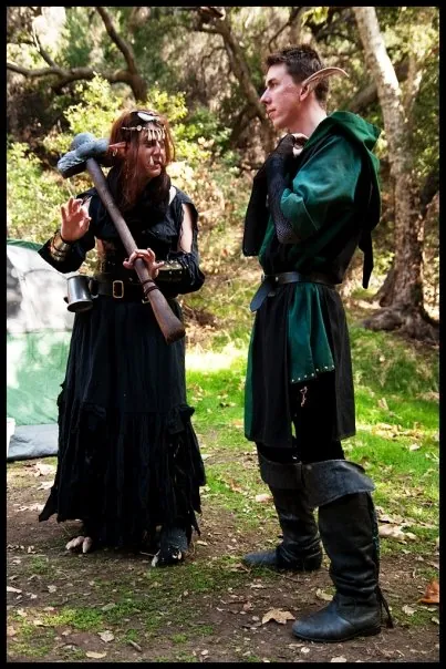 Two players in a forest, one in black with a horned headband and a war hammer, one in a green tunic with pointed ears